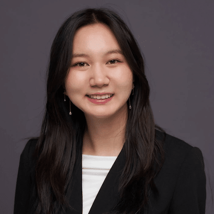 A woman with long dark hair, wearing a black blazer and white top, smiles at the camera against a plain dark background, reflecting the confidence she gained during her summer law internship at BRAWW Law.