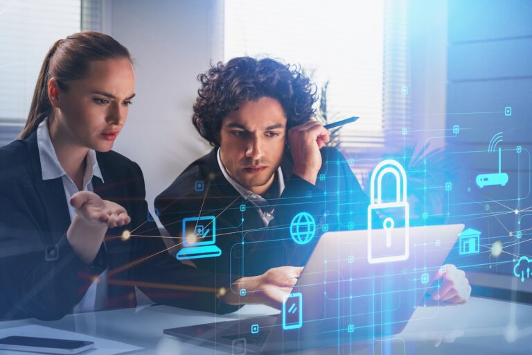 Two professionals at a desk look intently at a laptop screen with digital icons and a lock symbol overlay, representing cybersecurity or data protection.
